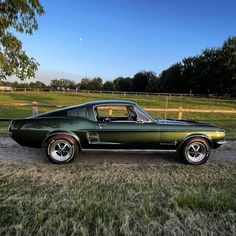 a green mustang sitting on top of a gravel road next to a lush green field