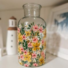 a glass vase with flowers painted on it sitting on a counter next to a lighthouse