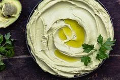 an avocado dip with cilantro and parsley in the middle on a wooden table