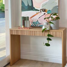 a wooden table topped with a potted plant next to a painting