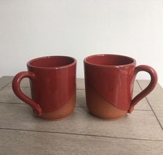 two red mugs sitting on top of a wooden table