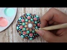 a person is holding a pencil and painting on a small button with flower designs in the center