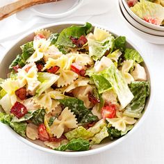 a white bowl filled with pasta salad next to a baguette on a table