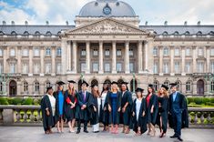 a group of people standing in front of a building wearing graduation gowns and caps