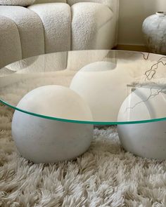 two white balls sitting on top of a glass table in front of a couch and chair