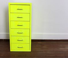 a yellow filing cabinet sitting on top of a hard wood floor next to a white wall