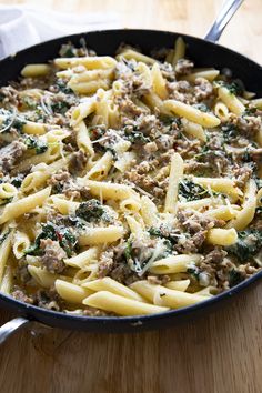 a skillet filled with pasta, meat and spinach on top of a wooden table