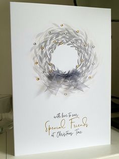 a christmas card with a wreath on the front and words written in gold ink, sitting on a table