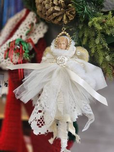 an angel ornament hanging from a christmas tree with pine cones in the background