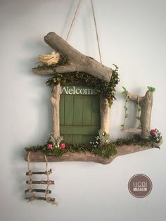 a welcome sign hanging on the wall next to a tree branch with flowers and vines