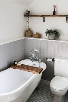 a white bathtub sitting next to a toilet in a bathroom under a shelf with plants