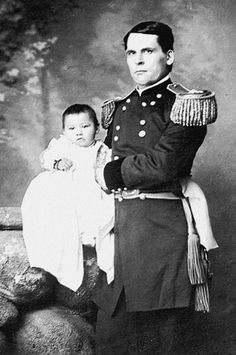 an old black and white photo of a man in uniform holding a baby