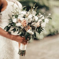 a woman holding a bouquet of white and pink flowers on her wedding day with greenery in the background