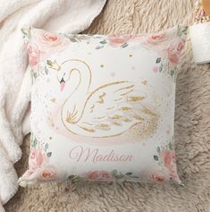 a white pillow with a gold swan on it next to a pink rose covered blanket