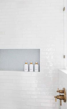 a white tiled bathroom with gold faucet and soap dispensers on the wall