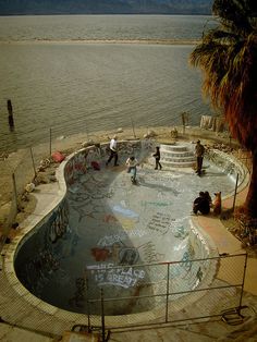 skateboarders skating in an empty swimming pool near the water with graffiti on it