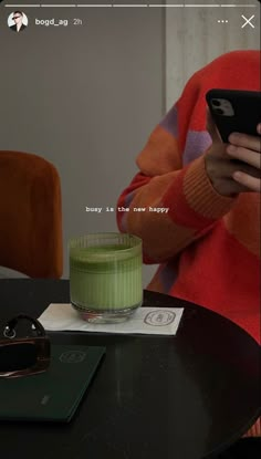 a person sitting at a table with a cell phone in their hand and a green cup next to it