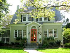 a house with a red door and green grass in the front yard, surrounded by trees