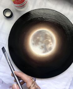 a person holding a pen in front of a black plate with the moon on it