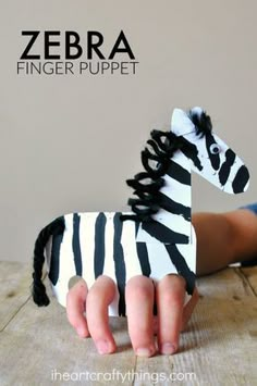 a zebra finger puppet sitting on top of a wooden table next to a child's hand