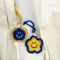 two crocheted smiley face keychains hanging from a white shirt with blue and yellow trim