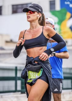 a woman in a black top and skirt running on the street with other people behind her