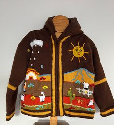 a brown sweater with farm animals on it and a sun in the sky, sitting on top of a wooden stand