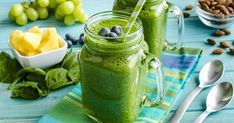 two mason jars filled with green smoothie and blueberries on top of a table