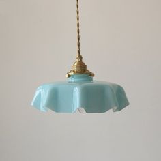 a blue light hanging from a ceiling with a white wall in the background and a gold lamp on top