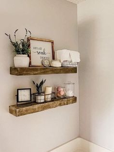 two wooden shelves with plants and candles on them in the corner of a white bathroom