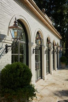 a white brick building with arched windows and lights on the outside wall next to a bush