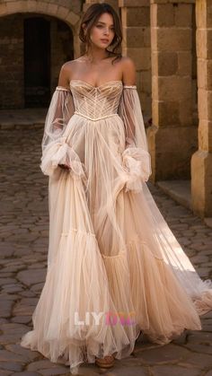 a woman in a long dress standing on a cobblestone street wearing an off the shoulder gown