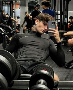 a man sitting in a gym holding up his cell phone to take a selfie