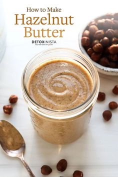 a jar filled with peanut butter next to nuts and spoons on a white table