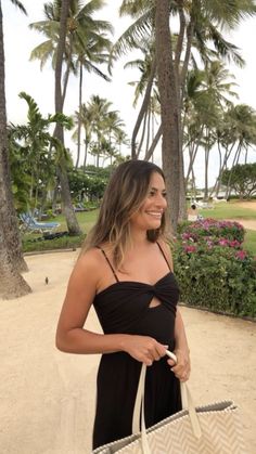 a woman in a black dress is holding a white bag and smiling at the camera