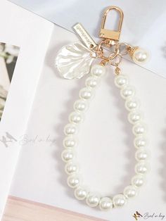 a white bracelet with pearls and a gold lock on it's end, sitting next to an open book