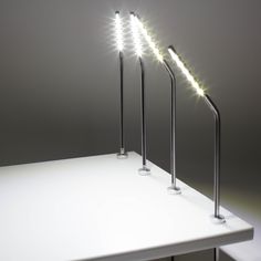 three lights that are sitting on top of a white table in front of a gray wall