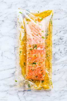 a piece of salmon wrapped in plastic on a marble counter top with herbs and seasoning