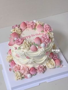 a white cake with pink flowers and berries on top is sitting on a card board