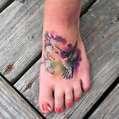 a woman's foot with a hummingbird tattoo on it