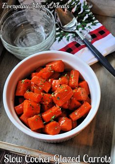 a white bowl filled with sliced carrots next to a fork and spoon on top of a wooden table