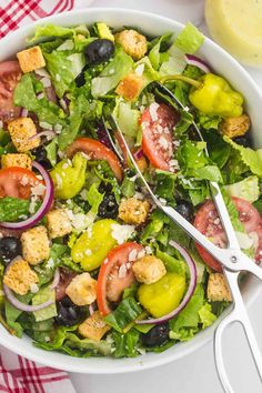 a salad with olives, tomatoes, lettuce and croutons