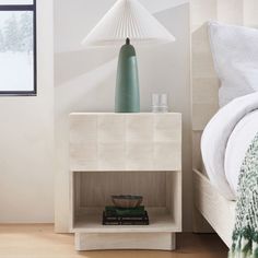 a bedroom with a bed, nightstand and lamp on the side table in front of it