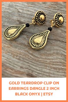 Gold teardrop clip-on earrings dangle. These pretty gold teardrop clip-on earrings dangle prettily from your ear lobes! The short earrings feature gold metalized drops that are hollow on the inside. They have an antique finish that is complemented with petite black onyx beads. The lightweight Gold Bohemian Clip-on Jewelry, Formal Gold Clip-on Teardrop Earrings, Bohemian Gold Clip-on Earrings, Gold Plated Teardrop Clip-on Jewelry, Brass Dangle Clip-on Earrings, Teardrop Brass Clip-on Earrings For Gift, Vintage Gold Teardrop Clip-on Earrings, Black Onyx Teardrop Earrings, Vintage Black Clip-on Earrings