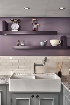 a kitchen with gray cabinets and white counter tops, along with shelves above the sink