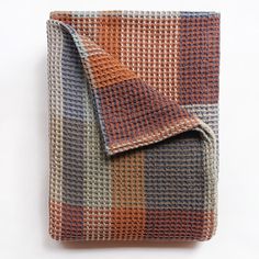 an orange, blue and grey checkered blanket folded on top of a white surface