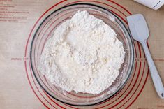 a glass bowl filled with white flour next to a measuring spoon on top of a table