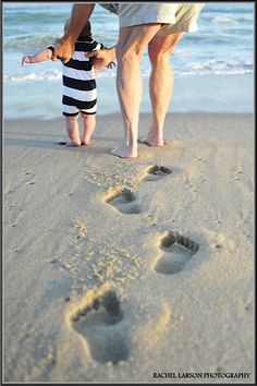 a father and son walking on the beach with their footprints in the sand as they hold each other's hand