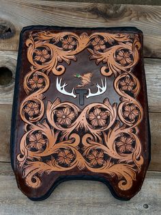 an intricately designed leather case with deer heads and flowers on the front, sitting on a wooden surface