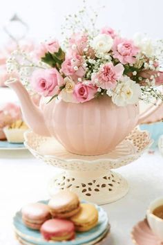 pink and white flowers in a teapot with macaroons on the plate next to it